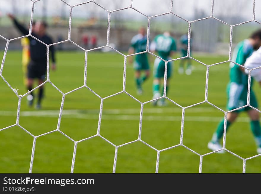 Football ground and football players through a grid of gate - an abstract dim background. Football ground and football players through a grid of gate - an abstract dim background.