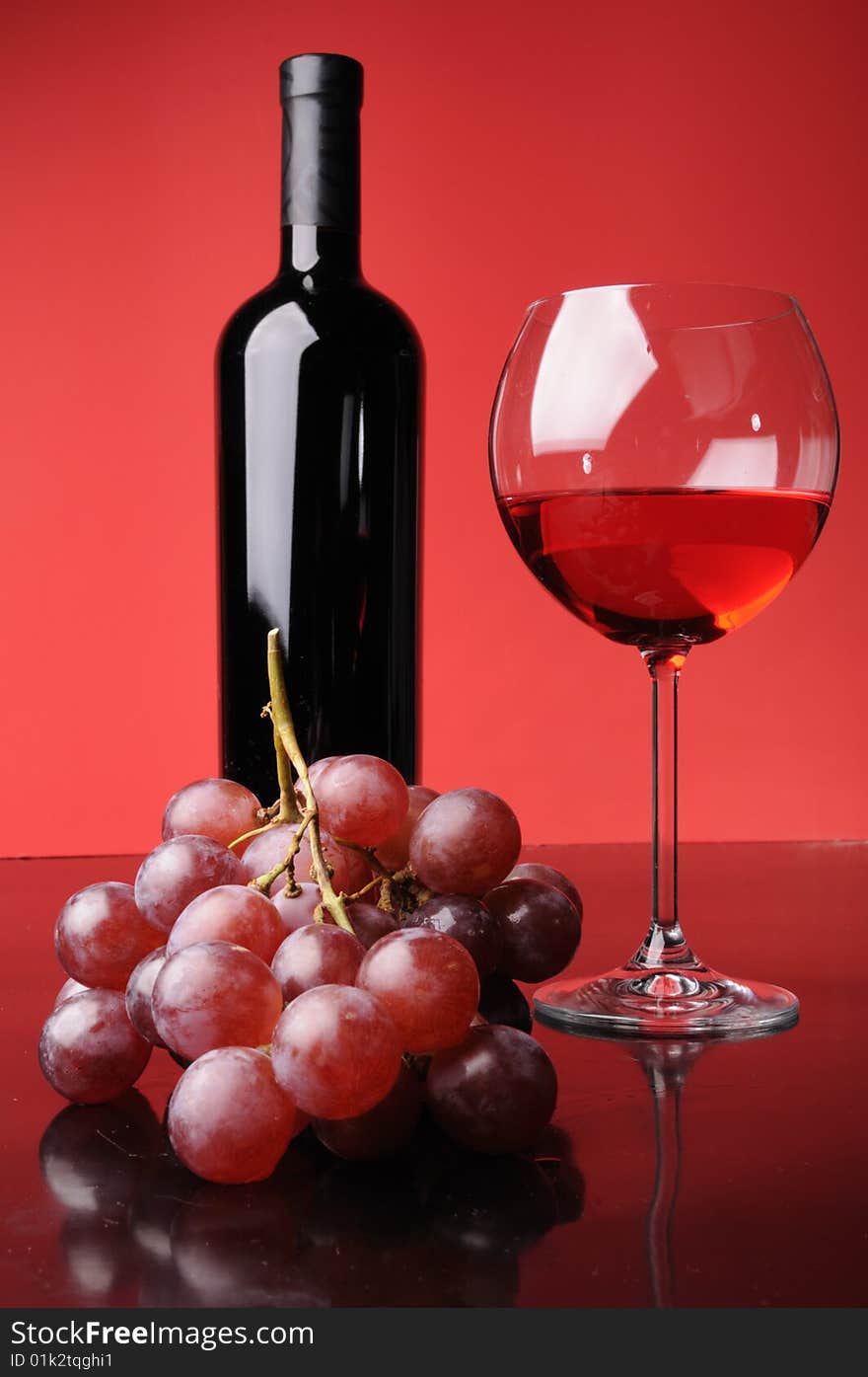 A glass and a bottle of wine with grapes