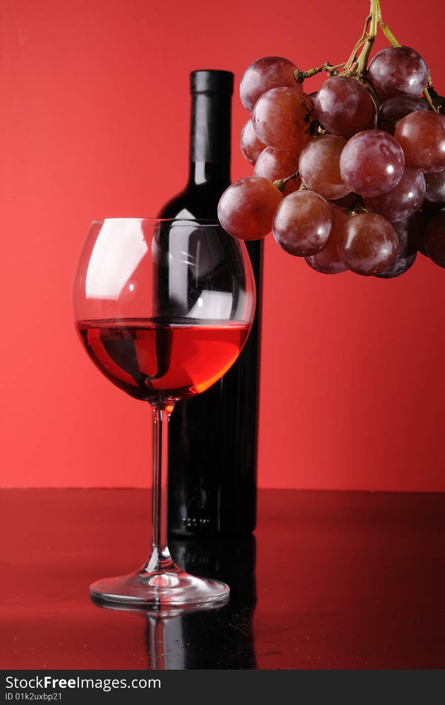 A glass and a bottle of wine with grapes