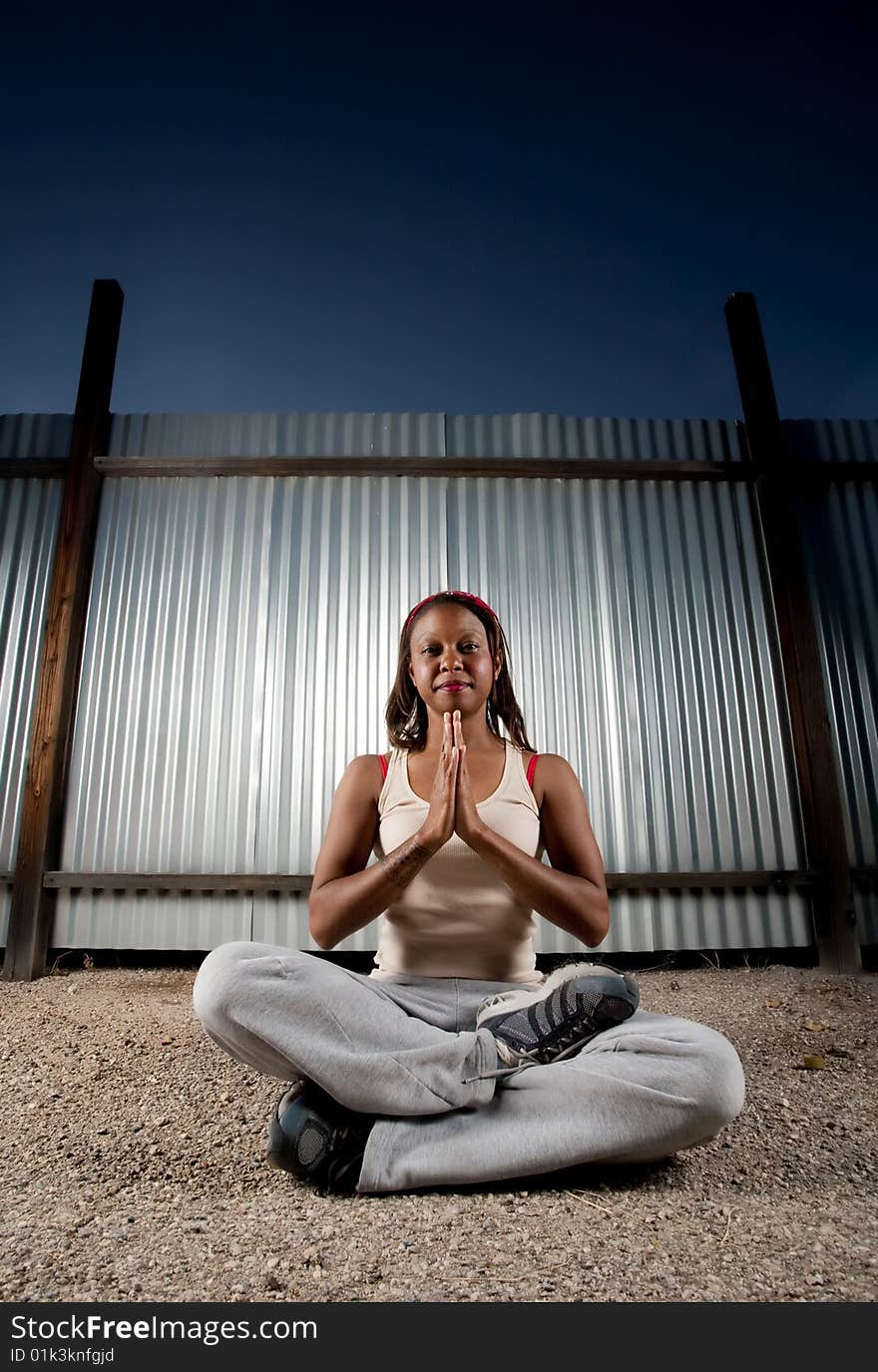 African-American woman meditating in front of corrugated metal