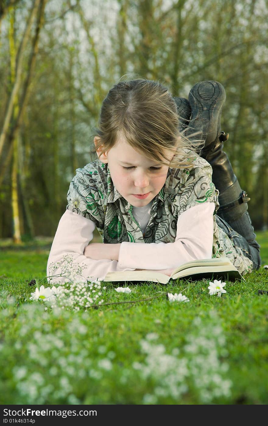 Girl reading book on grass in park.