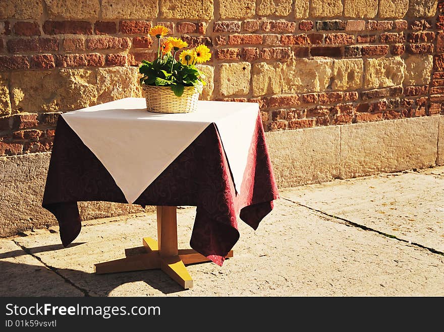 Lonely table with flowers against old brick wall in warm sunlight. The picture was made in Verona, Italy