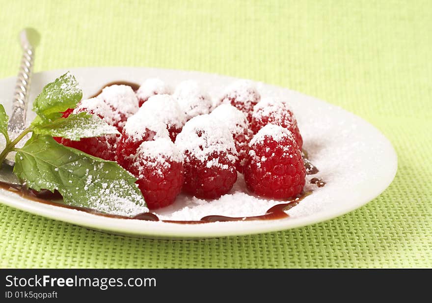 Fresh raspberry dessert served on a white plate, garnished with mint, chocolate sauce and icing sugar. Fresh raspberry dessert served on a white plate, garnished with mint, chocolate sauce and icing sugar