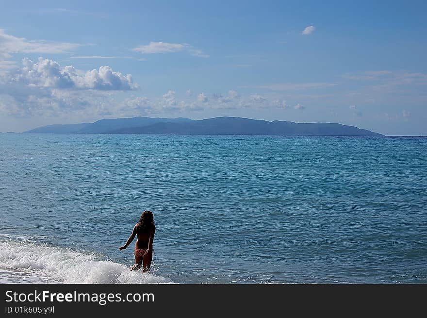 Exotic holiday: girl entering in blue sea facing blue island at the horizon