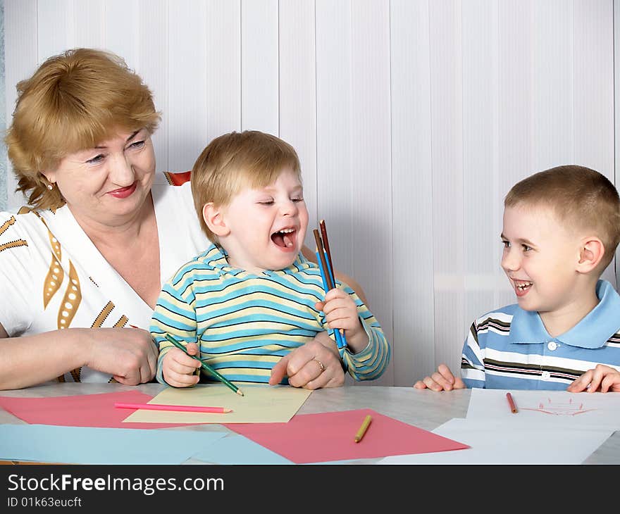 The grandmother is engaged in drawing with two grandsons. The grandmother is engaged in drawing with two grandsons