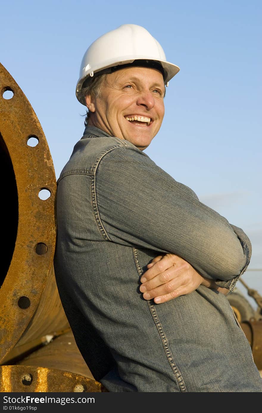 A portrait of a happy smiling construction worker leaning against large metal pipes. A portrait of a happy smiling construction worker leaning against large metal pipes.