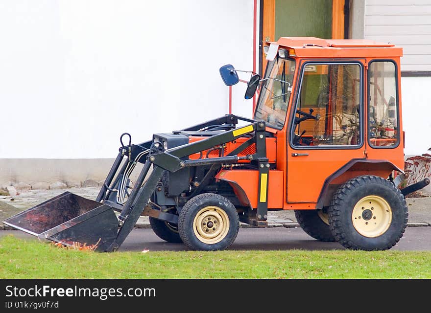 Orange Tractor With Scoop Bucket In The Suburbs