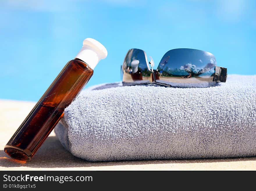 Sunglasses, towel and oil bottle by the swimming pool