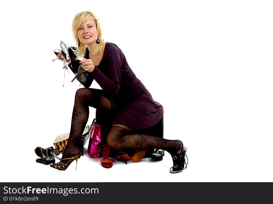 Full body view of lovely blond woman sitting on a pouf surrounded by lots of shopping bags and different shoes, trying on shoes, in elegant / business wear. Isolated on white background. Full body view of lovely blond woman sitting on a pouf surrounded by lots of shopping bags and different shoes, trying on shoes, in elegant / business wear. Isolated on white background.