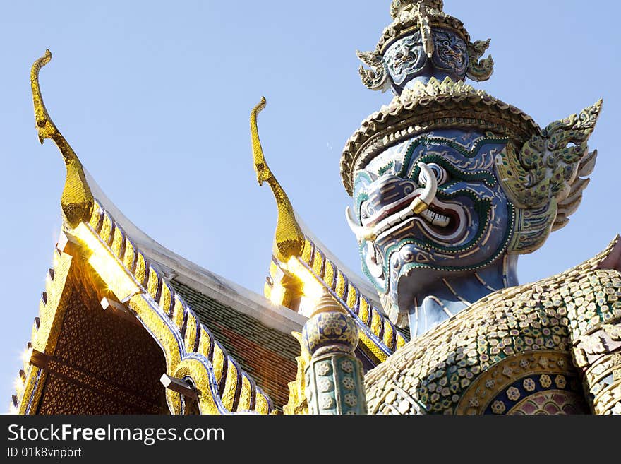 Closeup of a thai religious guardian icon with view of roof of buddhist shrines. Closeup of a thai religious guardian icon with view of roof of buddhist shrines