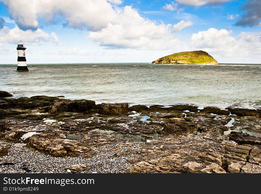 Puffin Island from the Isle of Anglesey with wave coming in over rocks with Penmon Lighthouse to the left