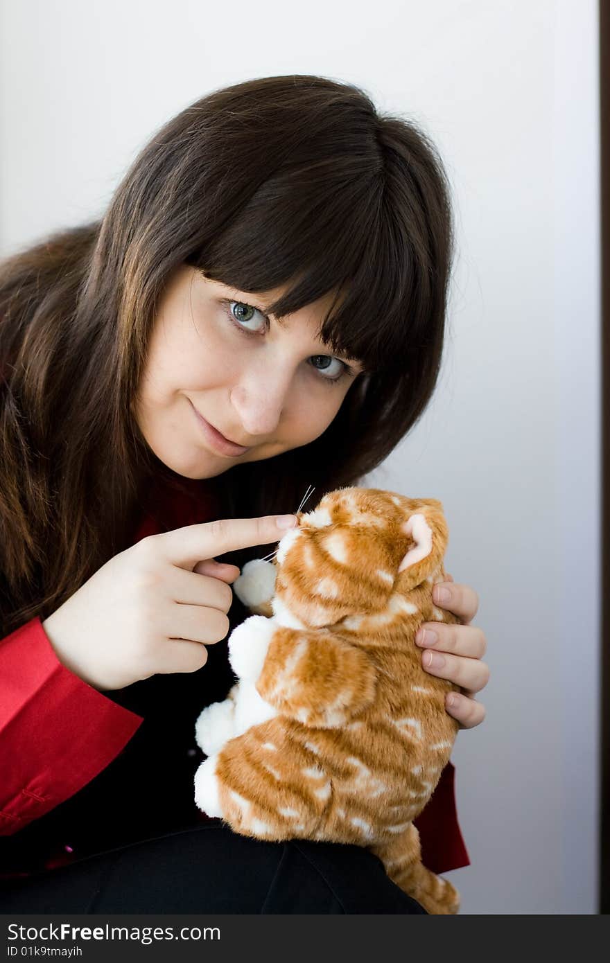 A girl holds a red  toy-kitten, and she touch nose with finger. A girl holds a red  toy-kitten, and she touch nose with finger