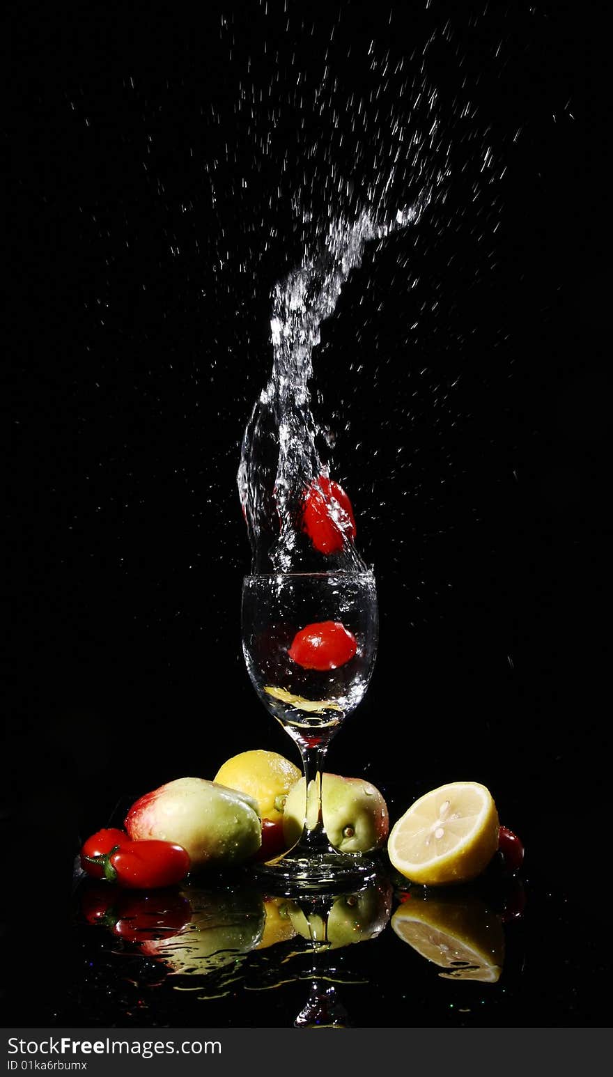 Blank background, red tomatos falling into water in a goblet, peach, tomatoes, lemon on the desk, with their reflection. Blank background, red tomatos falling into water in a goblet, peach, tomatoes, lemon on the desk, with their reflection