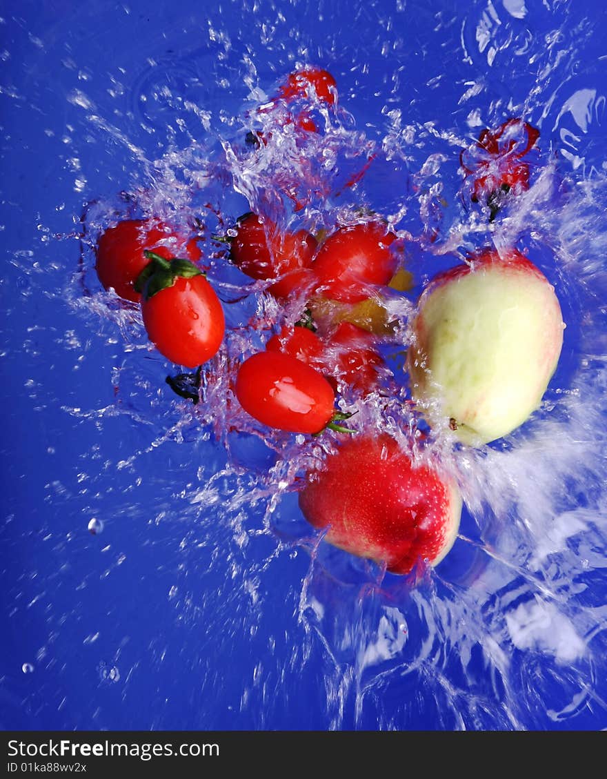 Red tomato, green and white peach,  faling into water over blue background. Red tomato, green and white peach,  faling into water over blue background.