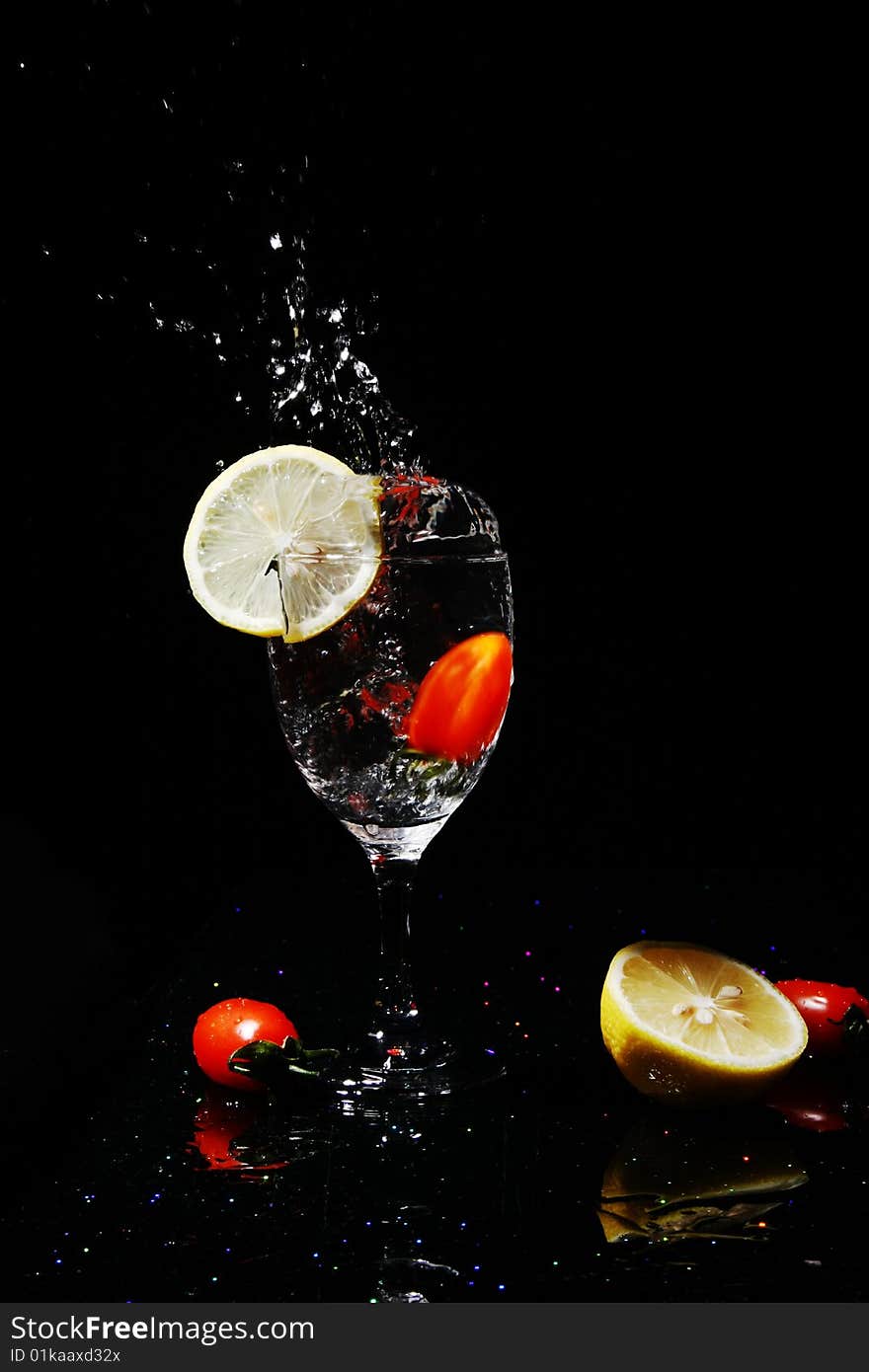 Blank background, red tomatos falling into water in a goblet, lemon, tomatoeson the desk, with their reflection. Blank background, red tomatos falling into water in a goblet, lemon, tomatoeson the desk, with their reflection