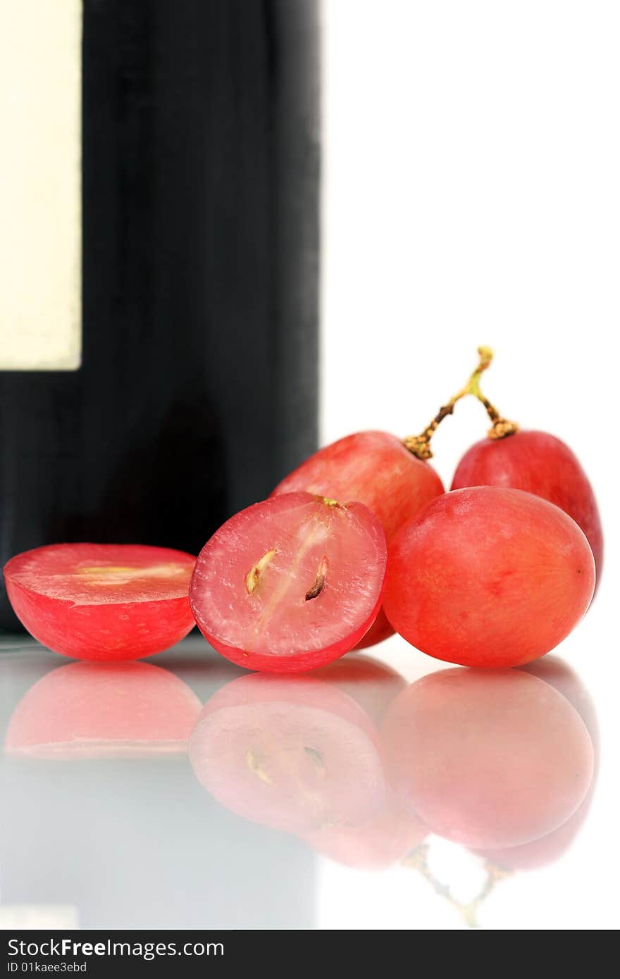 Bunch of red grapes on white plate beside wine bottle. Bunch of red grapes on white plate beside wine bottle.