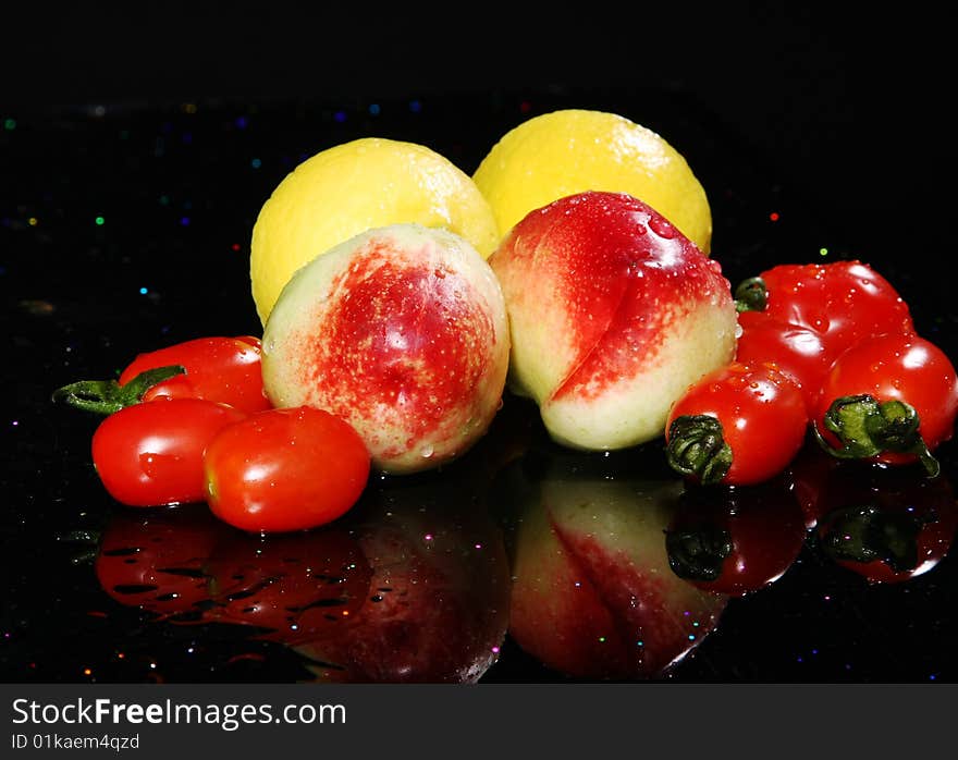 Lemon,s peachs and tomatoes on black background with reflection, yellow, red and green color. Lemon,s peachs and tomatoes on black background with reflection, yellow, red and green color