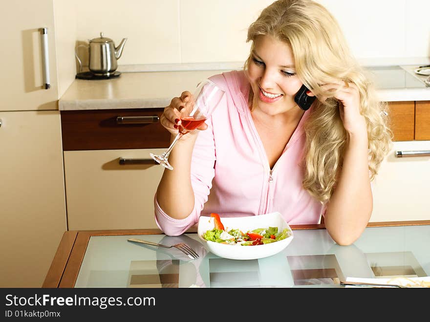 Beautiful blond girl at home in the kitchen eating salad and taking on the cellphone. Beautiful blond girl at home in the kitchen eating salad and taking on the cellphone