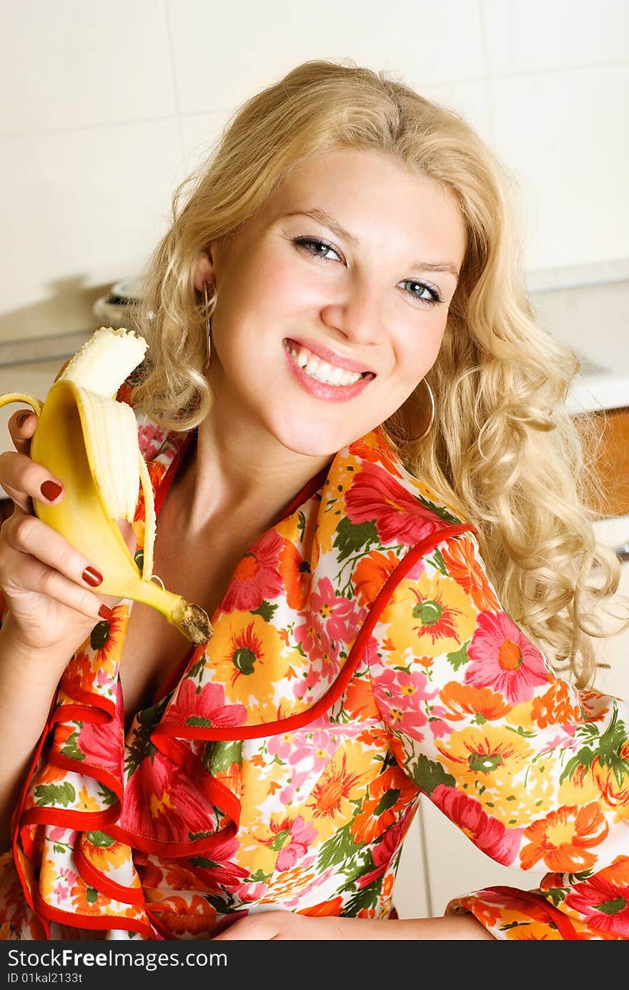 Beautiful happy girl at home in the kitchen eating a banana. Beautiful happy girl at home in the kitchen eating a banana