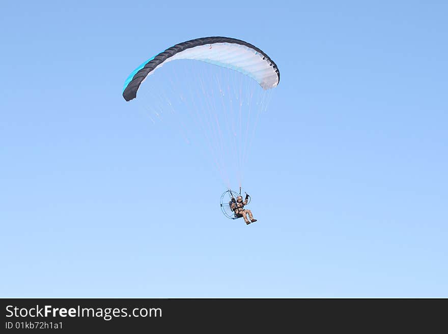 A multi-colored parachute holds up this paraplane on a clear blue day.