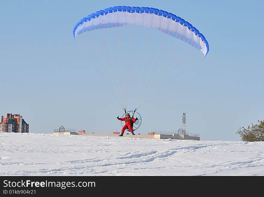 A multi-colored parachute holds up this paraplane on a clear blue day.