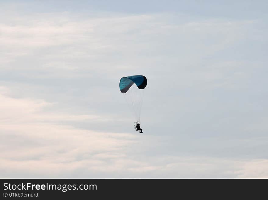 A multi-colored parachute holds up this paraplane on a clear blue day.