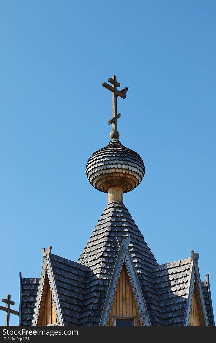 Wooden chapel roof with crow on the cross at sunny spring noon with blue sky. Wooden chapel roof with crow on the cross at sunny spring noon with blue sky