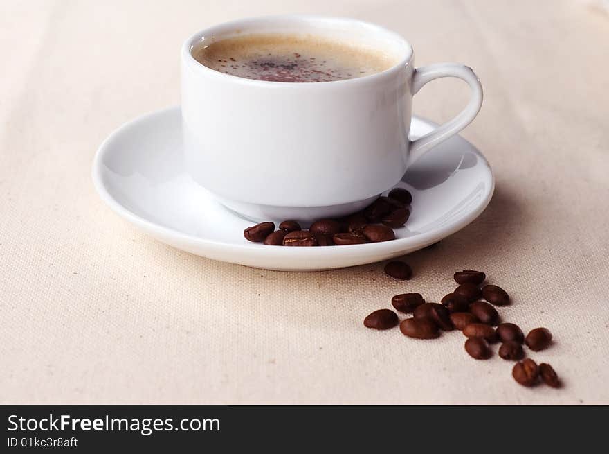 Cup of coffee with coffee beans on the tablecloth