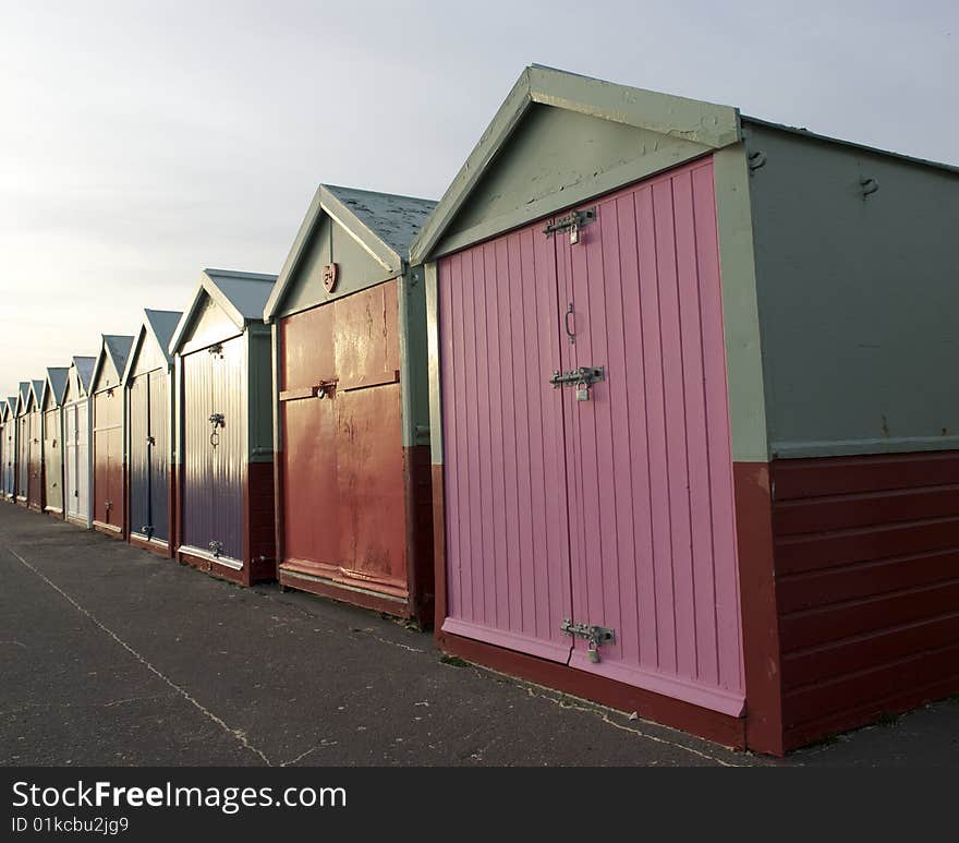 A long row of brightly painted traditional wooden beach huts on the the Sea Front at Brighton in the UK. Warm evening light reflects from the paint. A long row of brightly painted traditional wooden beach huts on the the Sea Front at Brighton in the UK. Warm evening light reflects from the paint