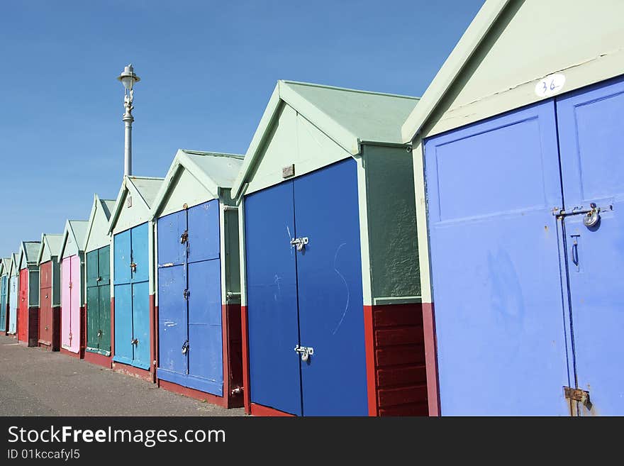 A row of brightly painted traditional wooden beach huts on the the Sea Front at Brighton in the UK. Midday Sunlight accentuates the blues and reds of the structures. A row of brightly painted traditional wooden beach huts on the the Sea Front at Brighton in the UK. Midday Sunlight accentuates the blues and reds of the structures