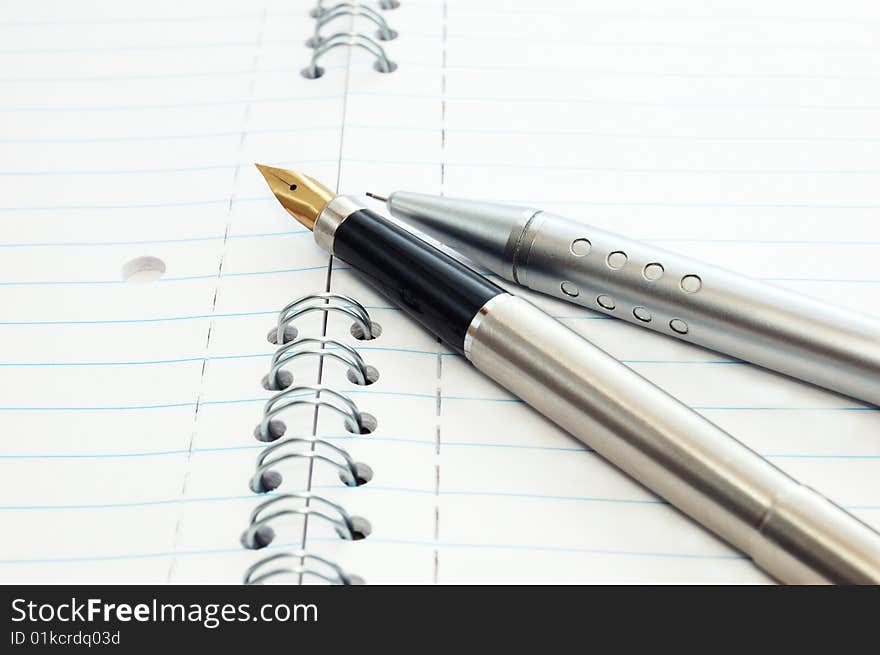 A gold pen and metal mechanical pencil on a spiral-bound notepad. A gold pen and metal mechanical pencil on a spiral-bound notepad