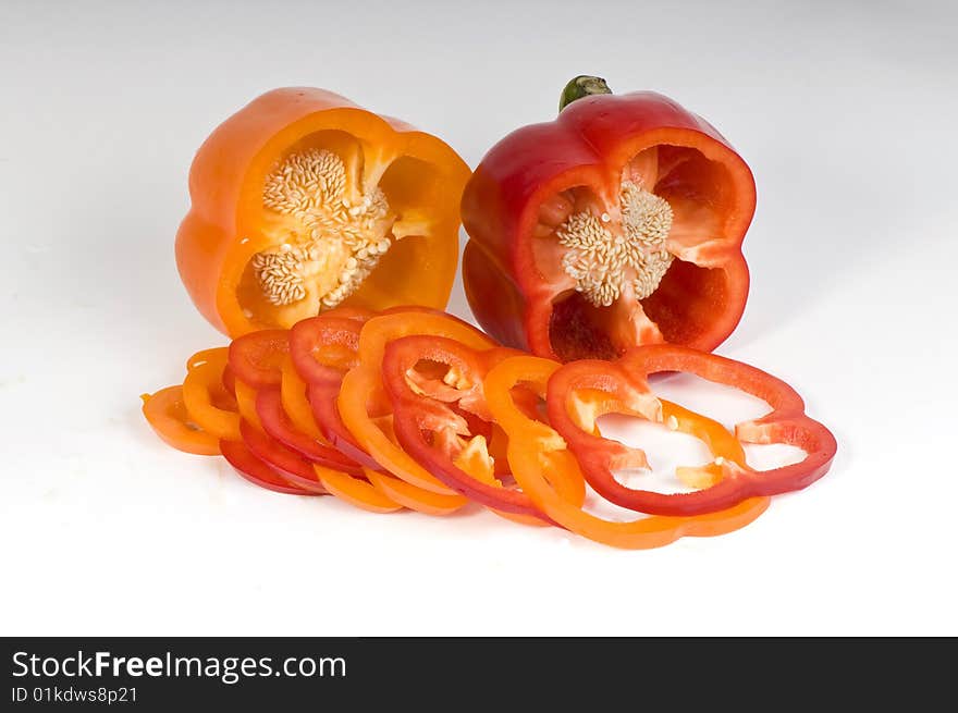 Cut orange and red sweet pepper showing seeds with slices on white