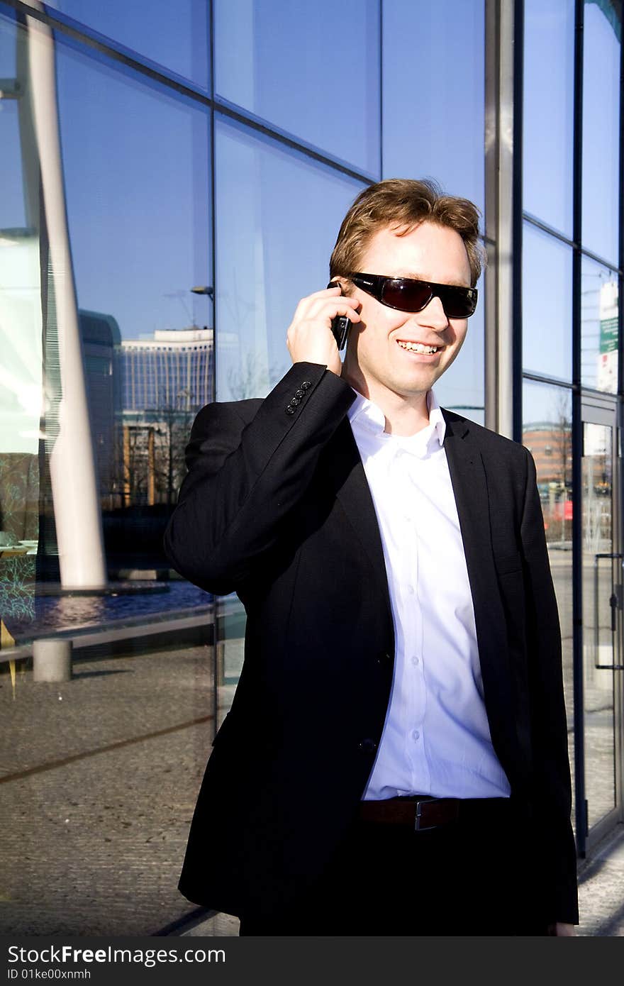 A young executive is speaking on the cell phone outside an office building of glass. A young executive is speaking on the cell phone outside an office building of glass.