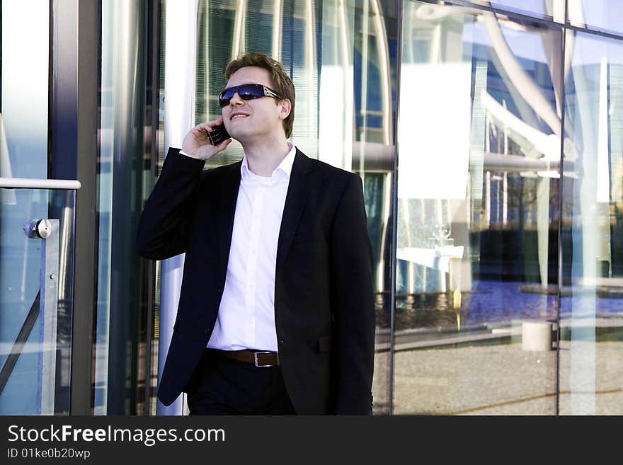 A young executive is speaking on the cell phone outside an office building of glass. A young executive is speaking on the cell phone outside an office building of glass.