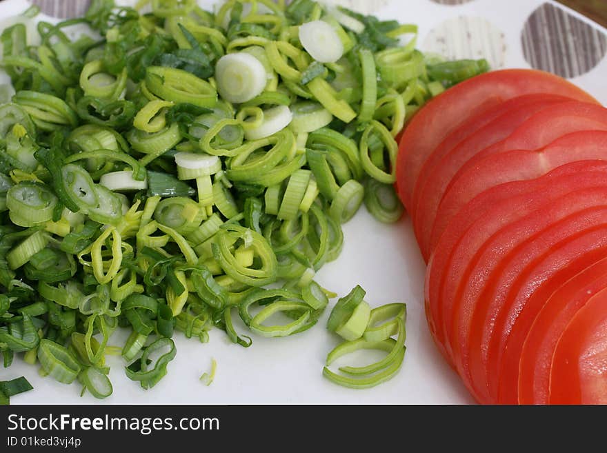 Plate contains some fresh vegetables, leek and tomatoes