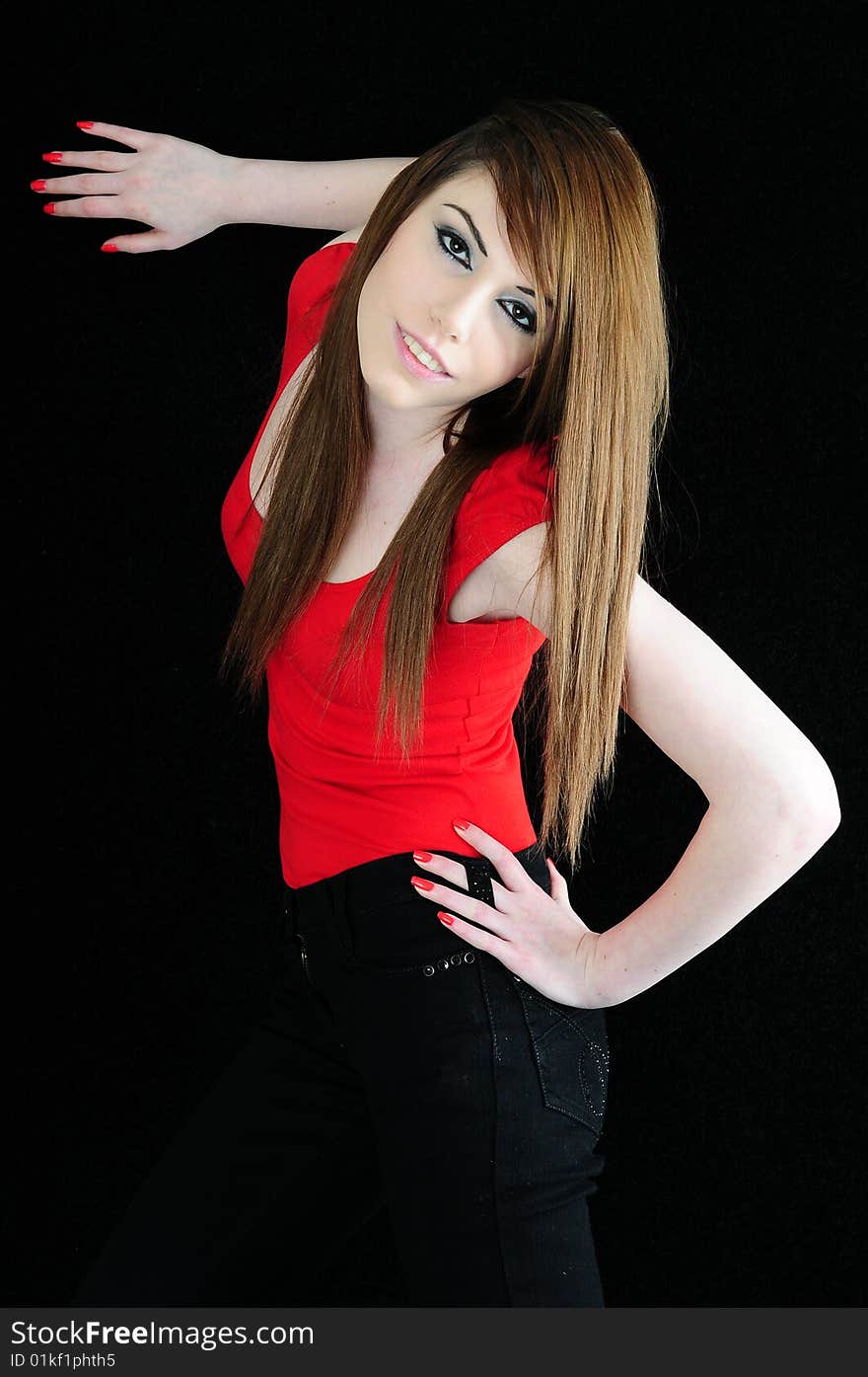 Female fashion model wearing a red top and black jeans with one hand on the black back drop and the other hooked into her jeans belt hole. Female fashion model wearing a red top and black jeans with one hand on the black back drop and the other hooked into her jeans belt hole.