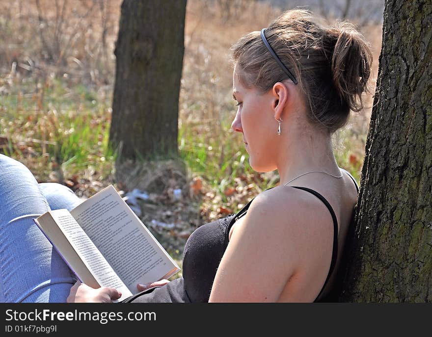 Girl reading a book outdoor, while sitting near the tree