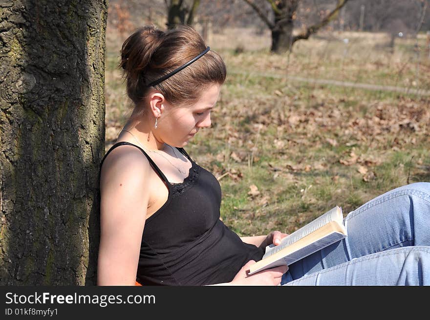 Girl reading a book outdoor, while sitting near the tree