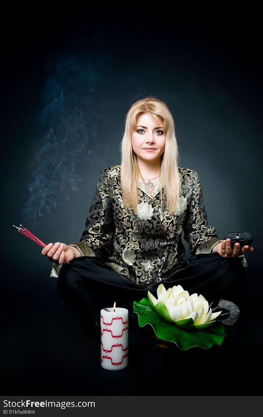 Woman meditating in lotus pose with aroma sticks, lotus, and candle