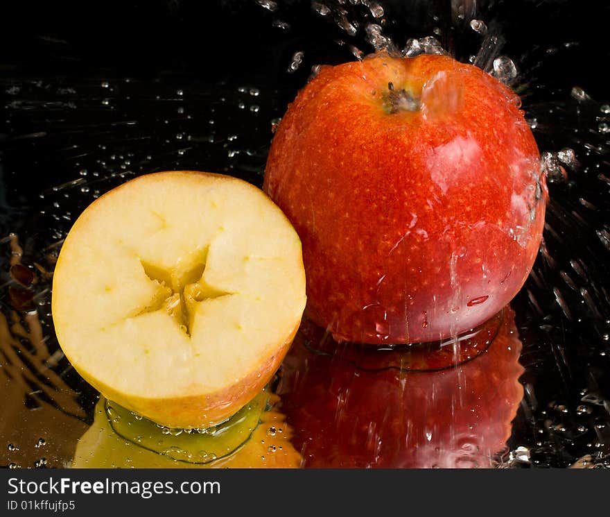 Full apple and half with water splashing on black