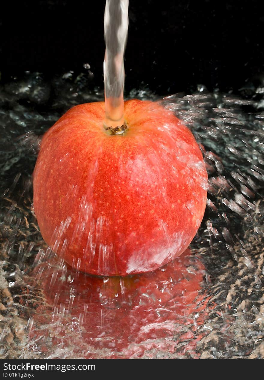 Red apple under water stream on black