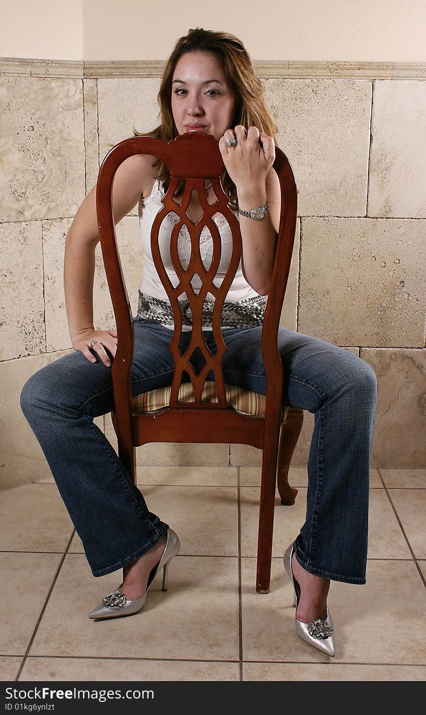 Model in jeans and heels straddles a chair in a tiled lobby.  She picked her silver bling to match her shoes. Model in jeans and heels straddles a chair in a tiled lobby.  She picked her silver bling to match her shoes.