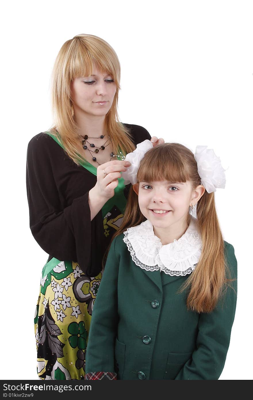 Mother is helping her's young daughter prepare to school. Woman is filleting ribbon on girl's hair. Mom is brushing young schoolgirl's hair. Isolated on white in studio. Mother is helping her's young daughter prepare to school. Woman is filleting ribbon on girl's hair. Mom is brushing young schoolgirl's hair. Isolated on white in studio.