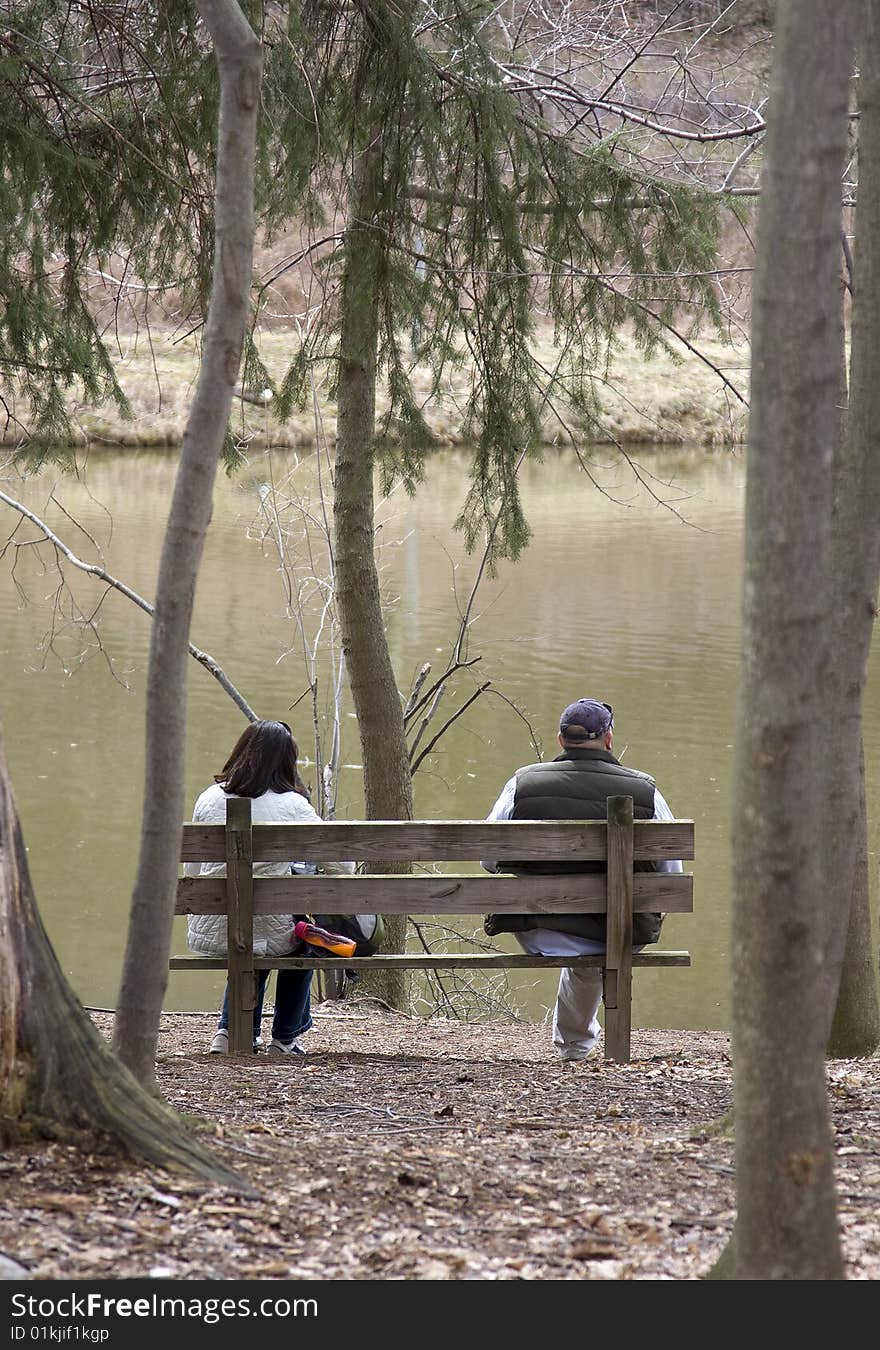 Heterosexual couple sitting on wood bench near pond. Heterosexual couple sitting on wood bench near pond