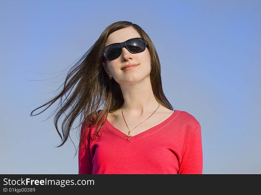 Closeup portrait of a beautiful young woman in sunglasses over big blue sky