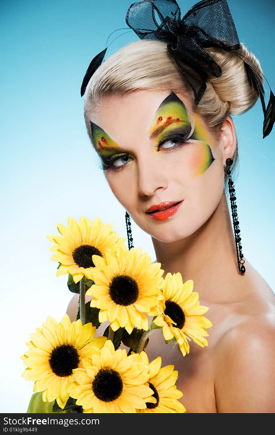 Young beauty with butterfly face-art and bouquet of sunflowers