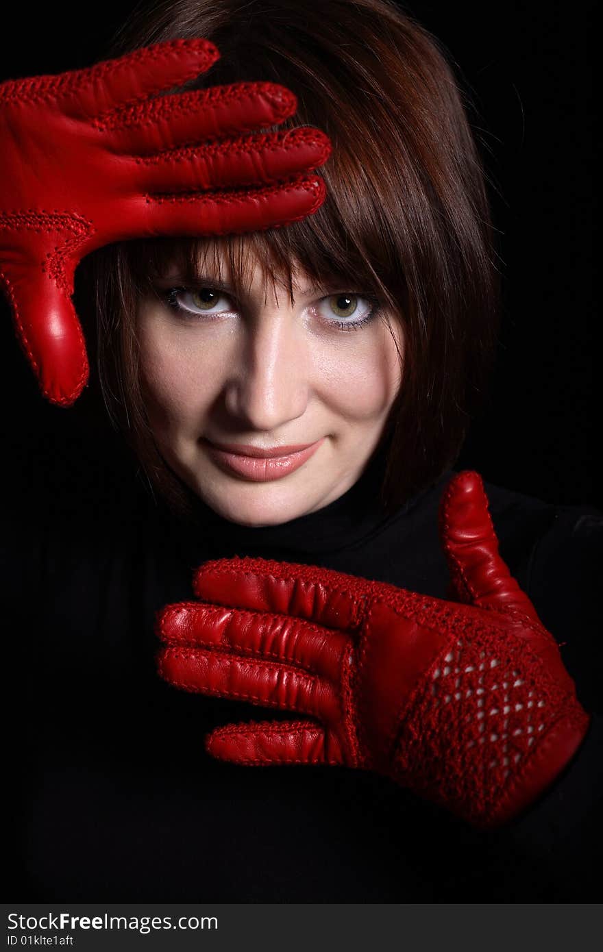 Woman looking straight from dark. In front of her red gloves on her hands. Vertical