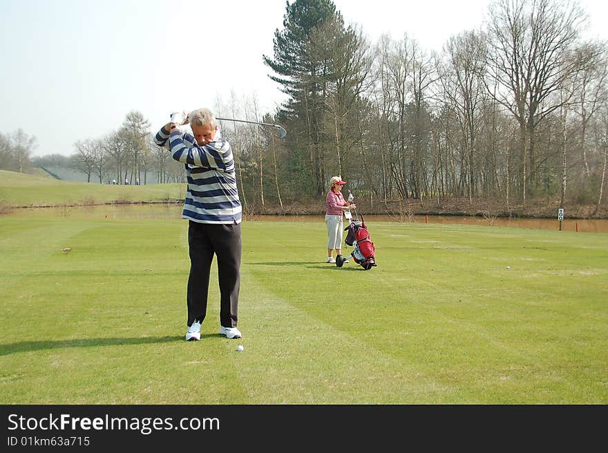 Male golfer teeing off, female golfer standing in the background