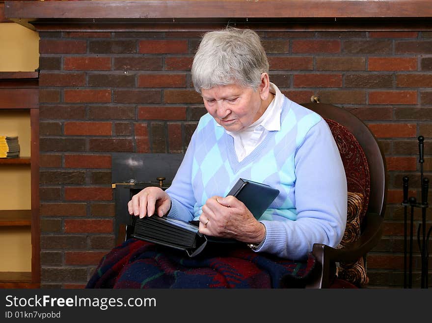 One elderly adult female sitting in a chair near the fireplace looking at a photo album. One elderly adult female sitting in a chair near the fireplace looking at a photo album