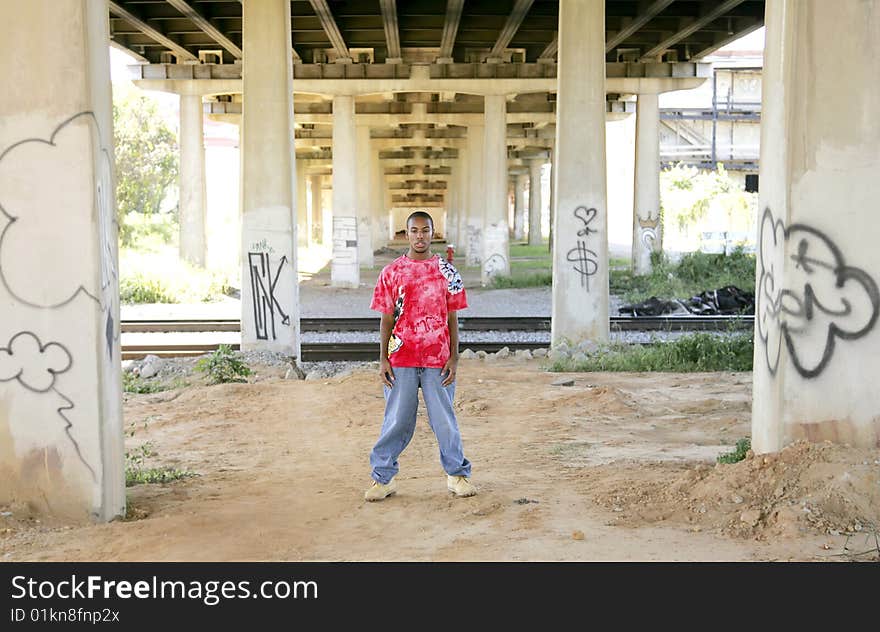 One young African American guy in a pink and red shirt standing near train tracks outside. One young African American guy in a pink and red shirt standing near train tracks outside